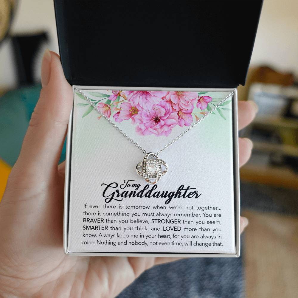 A hand holding a gift box with a ShineOn Fulfillment "To My Granddaughter, Always Keep Me In Your Heart" Love Knot Necklace in it.