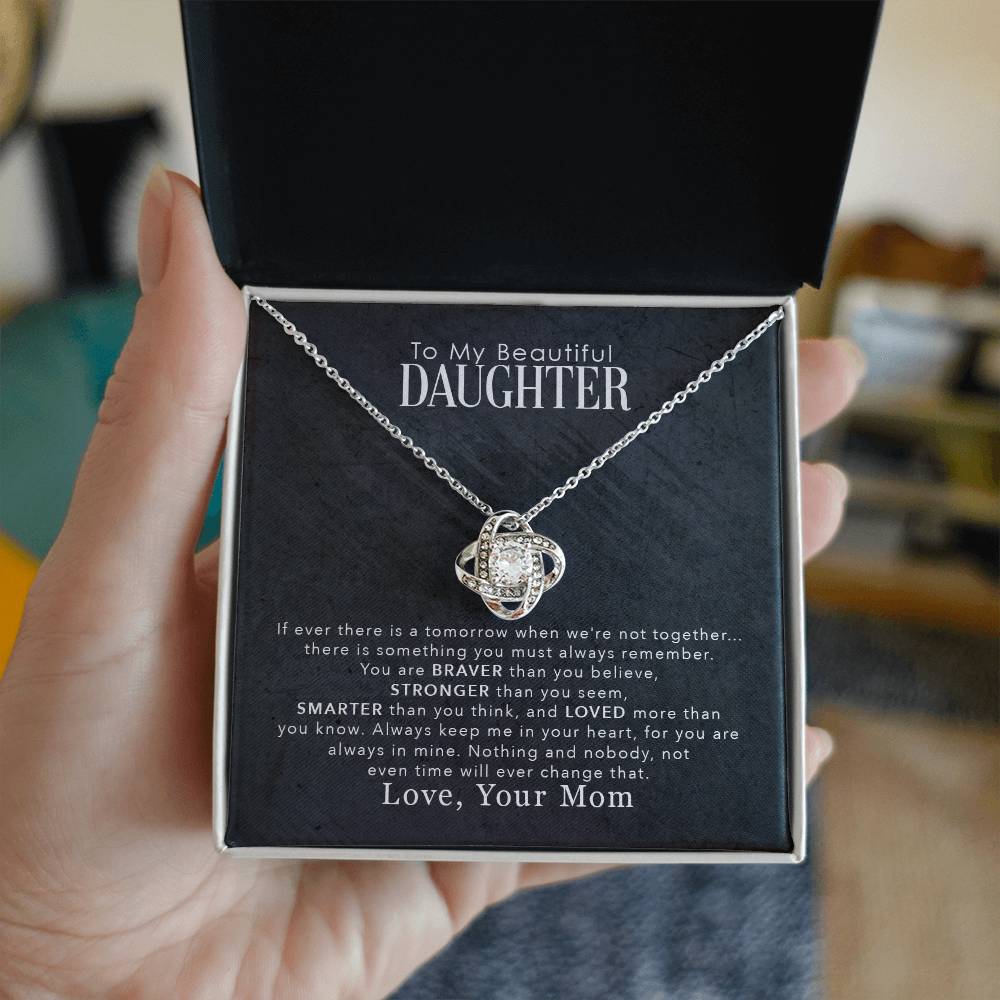 A hand gently cradling a sparkling To My Beautiful Daughter, You Are Braver Than You Believe - Love Knot Necklace pendant, nestled in a box adorned with cubic zirconia crystals. (Brand: ShineOn Fulfillment)