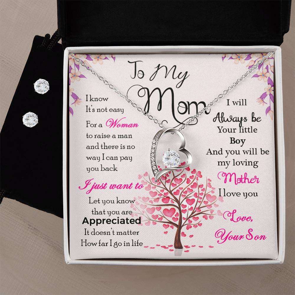 The "To My Mom, I Know It's Not Easy - Forever Love Necklace" by ShineOn Fulfillment comes elegantly packaged with a heartfelt message. This exquisite necklace and earring set features a heart-shaped pendant adorned with gem accents, crafted in a 14k white gold finish. The accompanying Cubic Zirconia earrings perfectly complement the Forever Love Necklace. The background showcases an illustration of a tree with pink heart-shaped leaves, symbolizing love and gratitude for mom.