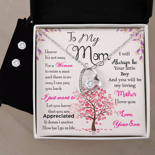 The "To My Mom, I Know It's Not Easy - Forever Love Necklace" by ShineOn Fulfillment comes elegantly packaged with a heartfelt message. This exquisite necklace and earring set features a heart-shaped pendant adorned with gem accents, crafted in a 14k white gold finish. The accompanying Cubic Zirconia earrings perfectly complement the Forever Love Necklace. The background showcases an illustration of a tree with pink heart-shaped leaves, symbolizing love and gratitude for mom.