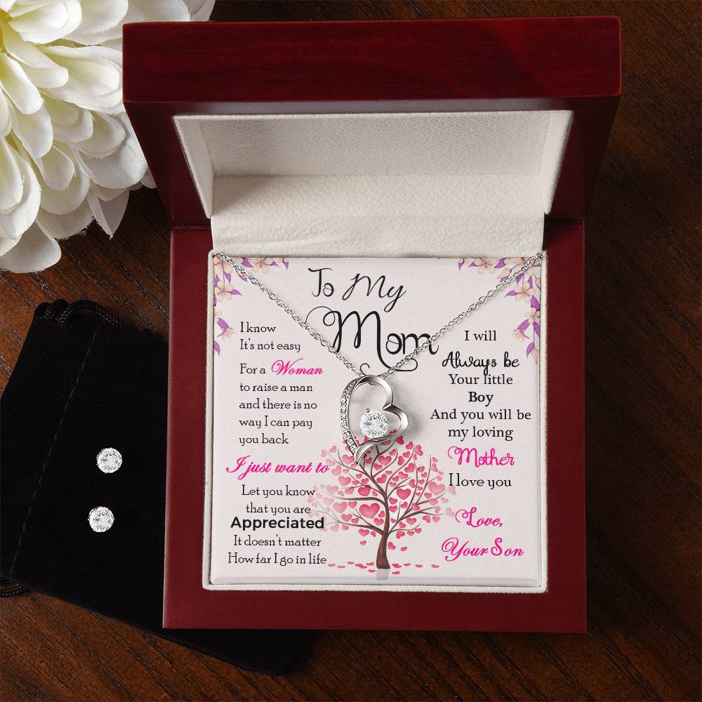 The "To My Mom, I Know It's Not Easy - Forever Love Necklace" from ShineOn Fulfillment features an elegant tree design and is beautifully presented in a wooden box. The box includes a heartfelt message from a son to his mom, conveying love and gratitude. Alongside the necklace, there is a Cubic Zirconia Earring Set and white flowers for added charm.