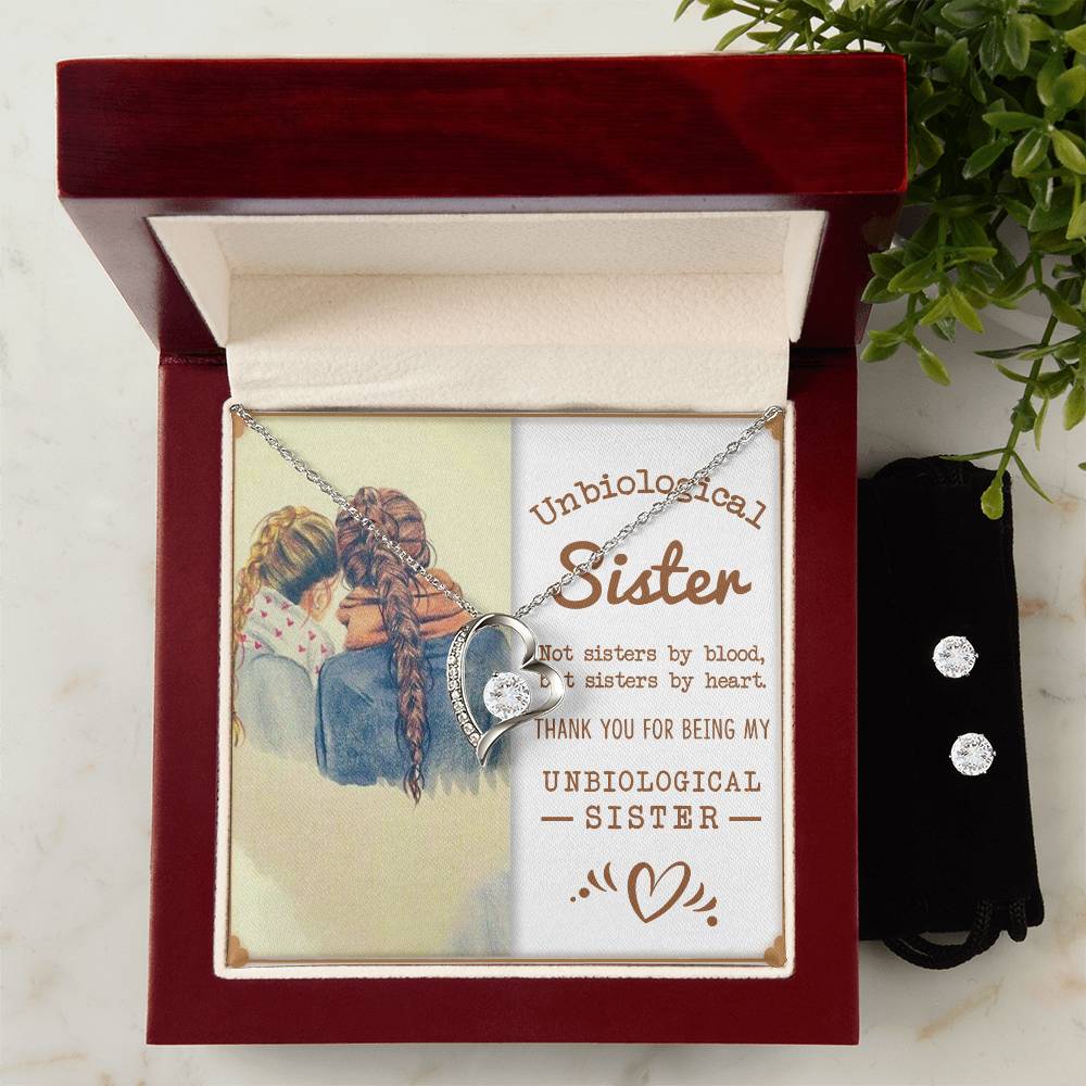 A beautiful silver Forever Love Necklace featuring a heart with an infinity symbol, known as the "To My Unbiological Sister, Sisters By Heart" by ShineOn Fulfillment, is elegantly placed in a wooden box. This box includes a touching message of gratitude addressed to an "Unbiological Sister." Alongside it sparkles a set of cubic zirconia earrings, surrounded by green leaves in the background.