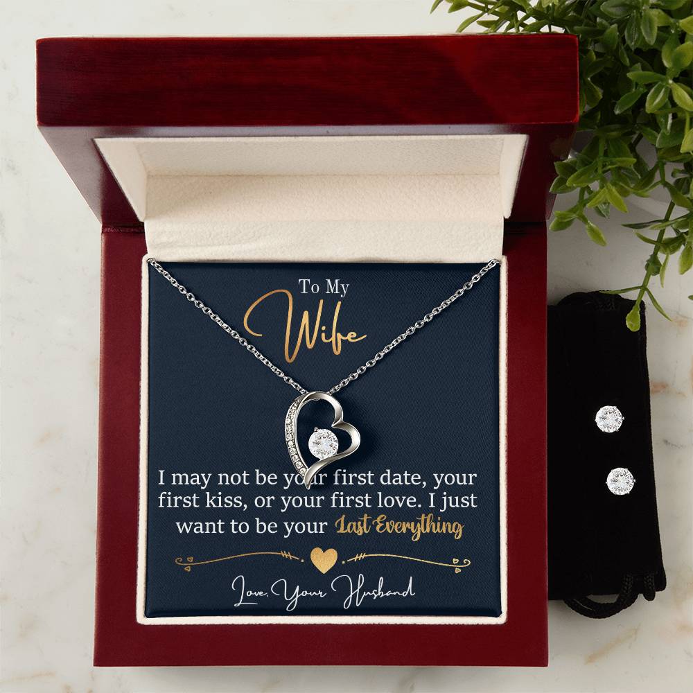 A Forever Love Necklace from ShineOn Fulfillment, featuring a crystal center and set in a 14k white gold finish, is elegantly displayed in a wooden box. Inside the box, there's a card that reads, "To My Wife: I may not be your first date... I just want to be your last everything. Love, Your Husband." Accompanying the jewelry box is a jewelry pouch.