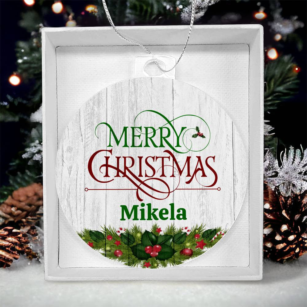 The Personalized Name Christmas Ornament from AnywherePOD, presented in a box, showcases the festive message "Merry Christmas Mikela" in decorative fonts. This unique keepsake features a holly and greenery motif at the base, set against a blurred background of a shimmering Christmas tree.