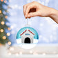 A person holding a AnywherePOD Dogs Name Christmas Ornament with a dog house on it.
