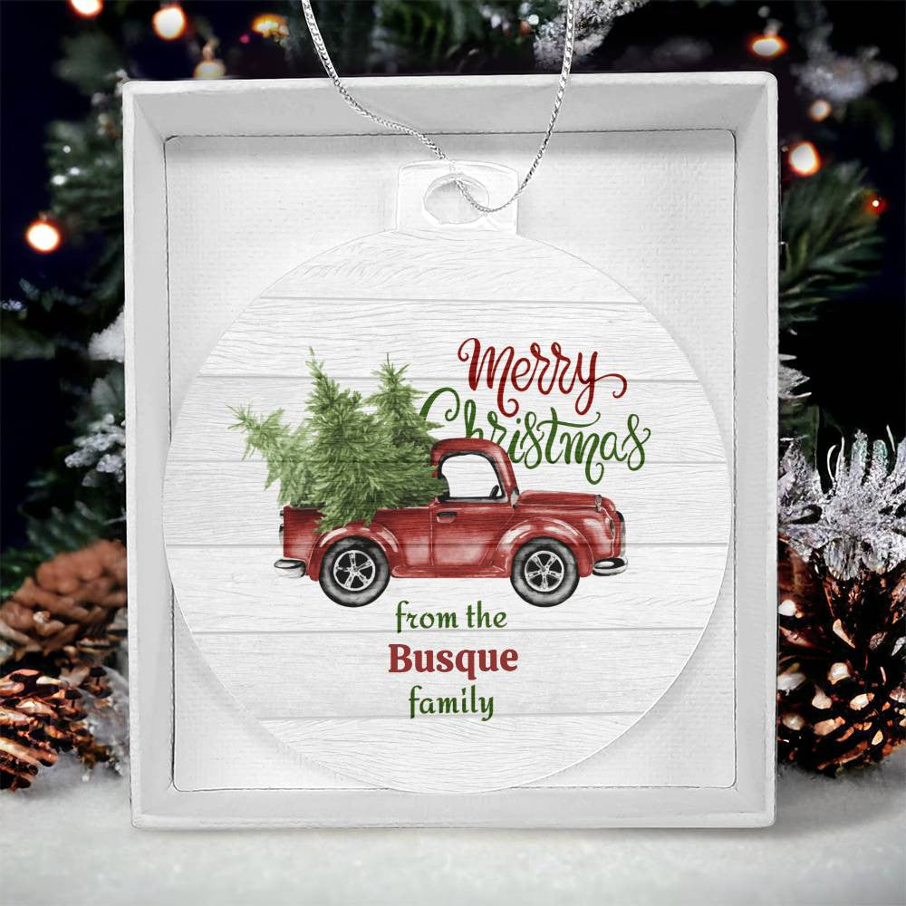 AnywherePOD's personalized acrylic ornament, featuring a vintage pickup truck with evergreen trees and the text "Merry Christmas from the Busque family," comes in a box set against a blurred background of a Christmas tree and decorations. The product is named "Personalized Old Pickup Truck Ornament with Christmas Trees – A Festive Holiday Keepsake!
