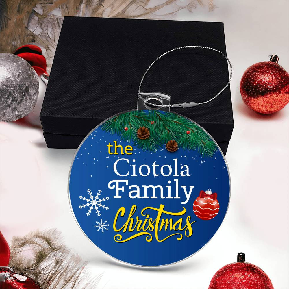 Introducing the AnywherePOD "Create Cherished Memories with a Personalized Family Name Christmas Ornament!" This exquisite round acrylic ornament boasts a blue background adorned with "The Ciotola Family Christmas" elegantly scripted in white and yellow. The design features intricate snowflakes, lush pine branches, charming pinecones, and a festive red ornament. Perfectly presented on a black box alongside red and silver baubles, this piece is sure to become a cherished holiday keepsake.