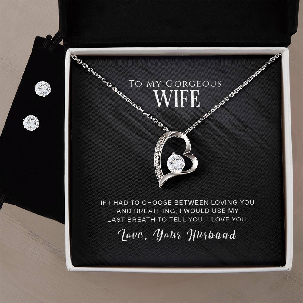 A heart-shaped necklace, named the "To My Wife, I Love You - Forever Love Necklace," crafted with a diamond and finished in 14k white gold by ShineOn Fulfillment, hangs elegantly in a jewelry box. Accompanying it is a touching message for a wife, signed "Love, Your Husband." Positioned to the side is the Cubic Zirconia Earring Set.