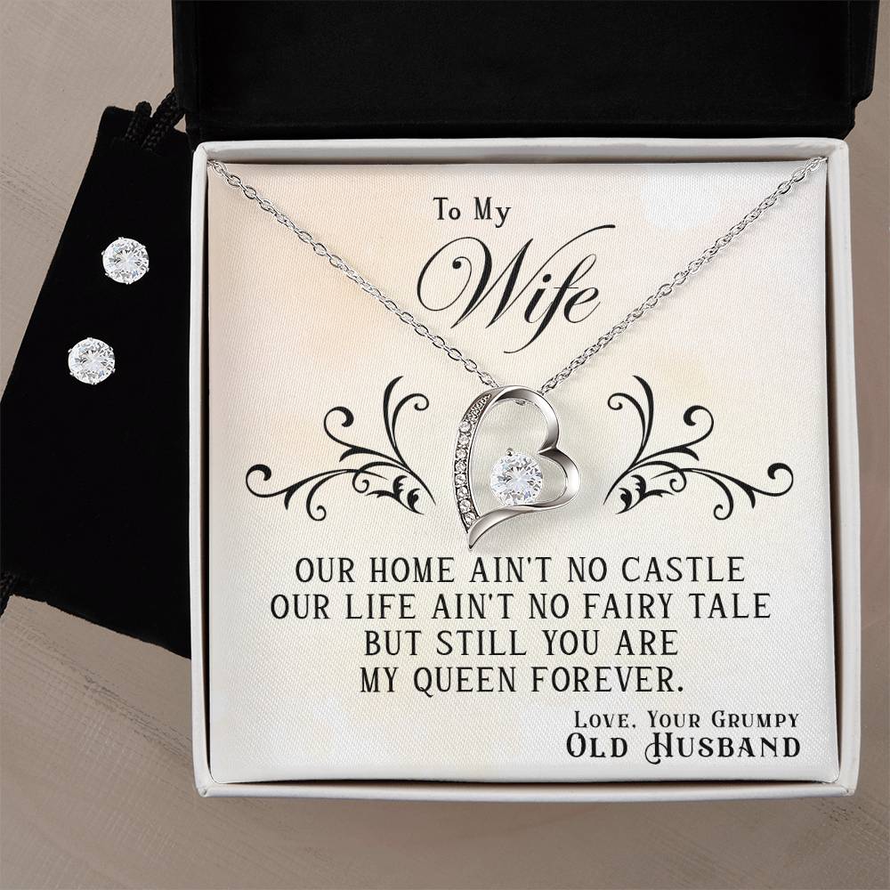 The ShineOn Fulfillment To My Wife, You Are My Queen Forever - Forever Love Necklace features a heart pendant adorned with a gemstone and is presented in an elegant box. The inside message reads: "To My Wife, Our home ain't no castle, our life ain't no fairy tale, but still you are my queen forever. Love, Your Grumpy Old Husband." This necklace includes a 14k white gold finish for timeless charm.