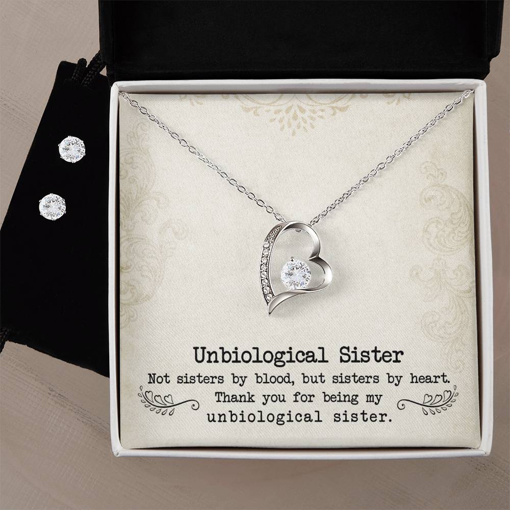 A Forever Love Necklace from ShineOn Fulfillment, designed in a heart shape and adorned with a crystal, is elegantly presented in an open box next to a Cubic Zirconia Earring Set. The lining of the box reads, "To My Unbiological Sister - Sister By Heart. Not sisters by blood, but sisters by heart. Thank you for being my unbiological sister.