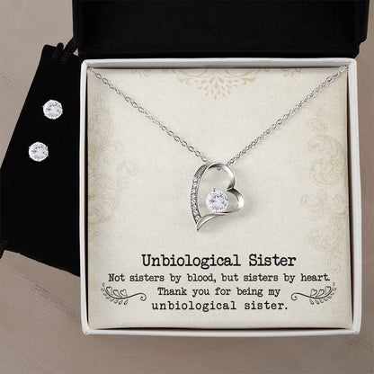 A Forever Love Necklace from ShineOn Fulfillment, designed in a heart shape and adorned with a crystal, is elegantly presented in an open box next to a Cubic Zirconia Earring Set. The lining of the box reads, "To My Unbiological Sister - Sister By Heart. Not sisters by blood, but sisters by heart. Thank you for being my unbiological sister.