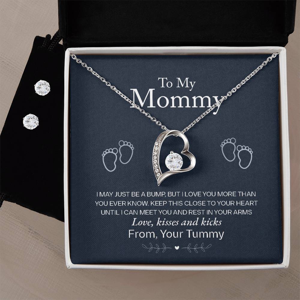 A heartfelt gift from ShineOn Fulfillment features the "To My Mommy, Love From Your Tummy - Forever Love Necklace" adorned with a central diamond in a 14k white gold finish, nestled on a message card inside a black box. The card reads: "To My Mommy" from an unborn baby. Accompanying the necklace are elegant Cubic Zirconia stud earrings.