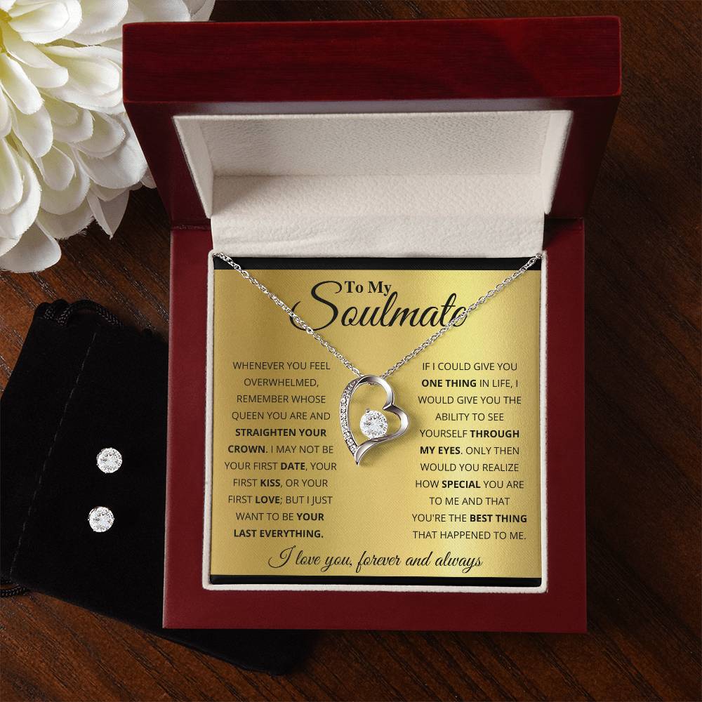 A jewelry gift box showcases the "To My Soulmate, You’re The Best Thing That Happened To Me - Forever Love Necklace" by ShineOn Fulfillment. The necklace features two interlocking circles with a gemstone set in a 14k white gold finish, accompanied by a touching message to a soulmate. Next to the box is a small black pouch containing a Cubic Zirconia Earring Set, and part of a white flower can be seen.