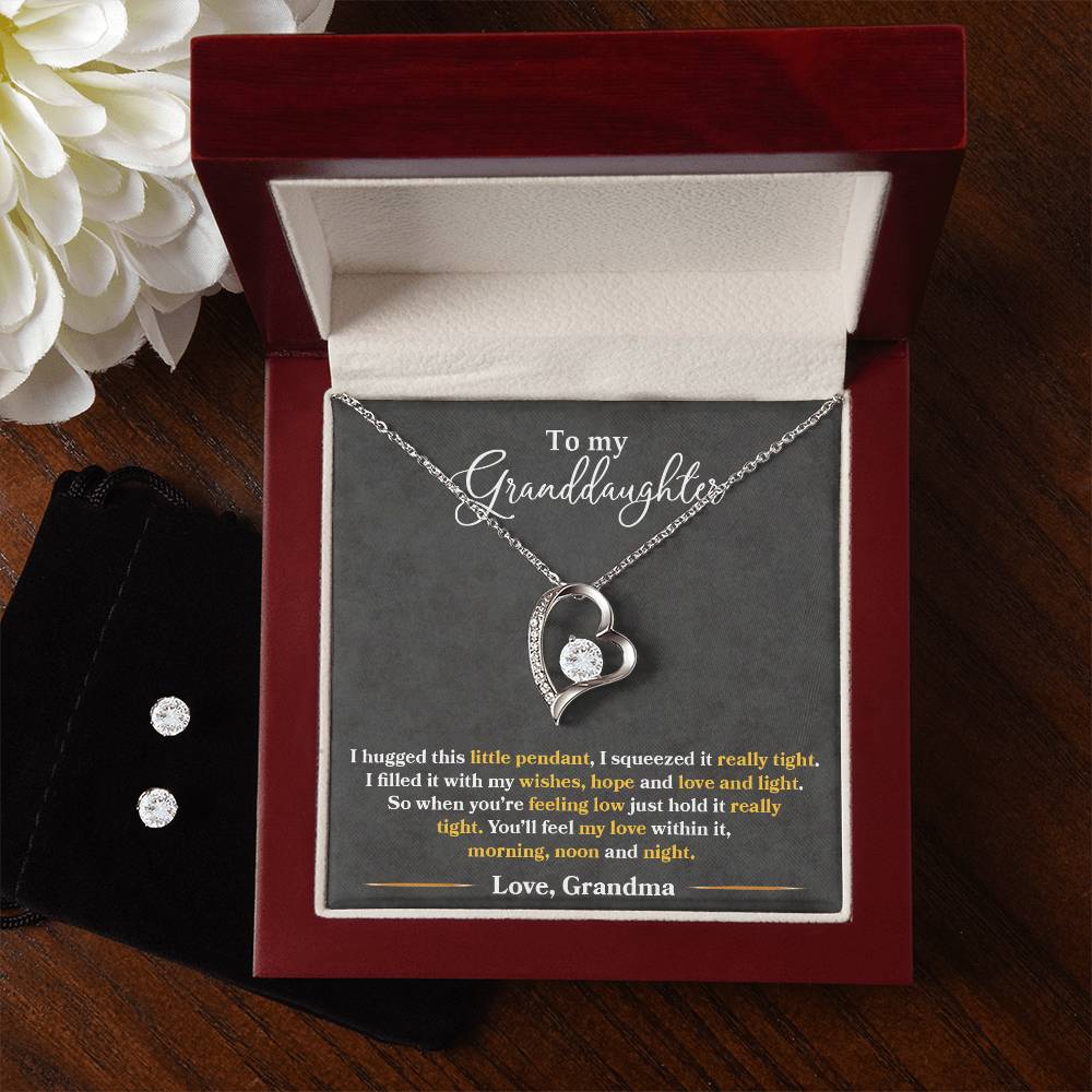 An open jewelry box showcases the ShineOn Fulfillment's "To My Granddaughter, You'll Feel My Love Within This - Forever Love Necklace," finished in 14k white gold and shaped like a heart, capturing the light's reflection. The lid features a heartfelt message from a grandmother to her granddaughter. Nearby, a small pouch holds a set of Cubic Zirconia Earrings that beautifully complement the necklace.