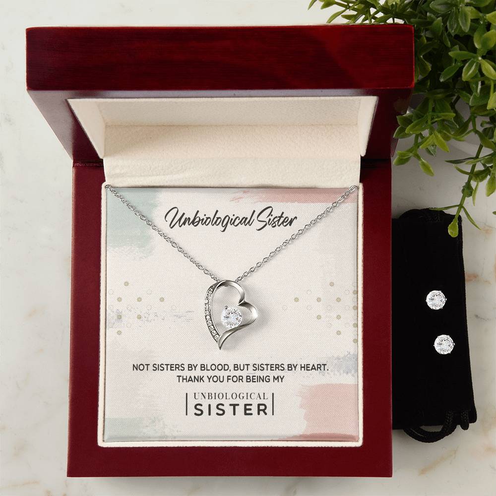 As the jewelry box opens, it unveils the "To My Unbiological Sister, Thank You - Forever Love Necklace" by ShineOn Fulfillment, featuring a heart-shaped pendant on an elegant chain with a central gemstone enclosed in a 14k white gold finish. Accompanying this symbol of eternal love is a pair of cubic zirconia earrings. The lid reads: "Unbiological Sister. Not sisters by blood, but sisters by heart.