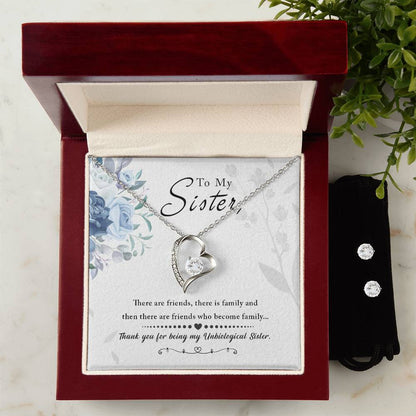 The ShineOn Fulfillment "To My Sister, Thank You For Everything - Forever Love Necklace," featuring a heart shape and 14k white gold finish, is elegantly displayed in a red velvet box alongside a heartfelt message card reading "To My Sister." Next to it, the Cubic Zirconia Earring Set is nestled in a black pouch. The scene is beautifully complemented by surrounding green plant leaves.