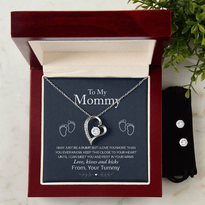 The "To My Mommy, Love From Your Tummy - Forever Love Necklace" by ShineOn Fulfillment features a stunning silver heart pendant with a central gem and 14k White Gold Finish, beautifully presented in a red velvet jewelry box. Accompanying the Forever Love Necklace is a touching message for a mother from her unborn child, surrounded by tiny footprints. In addition to this heartfelt piece, there's also a brilliant set of Cubic Zirconia Earrings nearby.