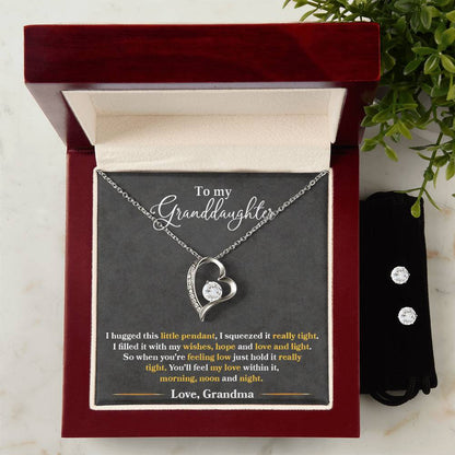 Upon opening the box, you'll find a ShineOn Fulfillment "To My Granddaughter, You'll Feel My Love Within This" Forever Love Necklace. It features a heart-shaped pendant with a circular gemstone and is finished in stunning 14k white gold. Inside, it bears the message "To my Granddaughter," followed by a touching note from Grandma. Alongside the necklace is an elegant Cubic Zirconia Earring Set, adding to the thoughtful presentation.