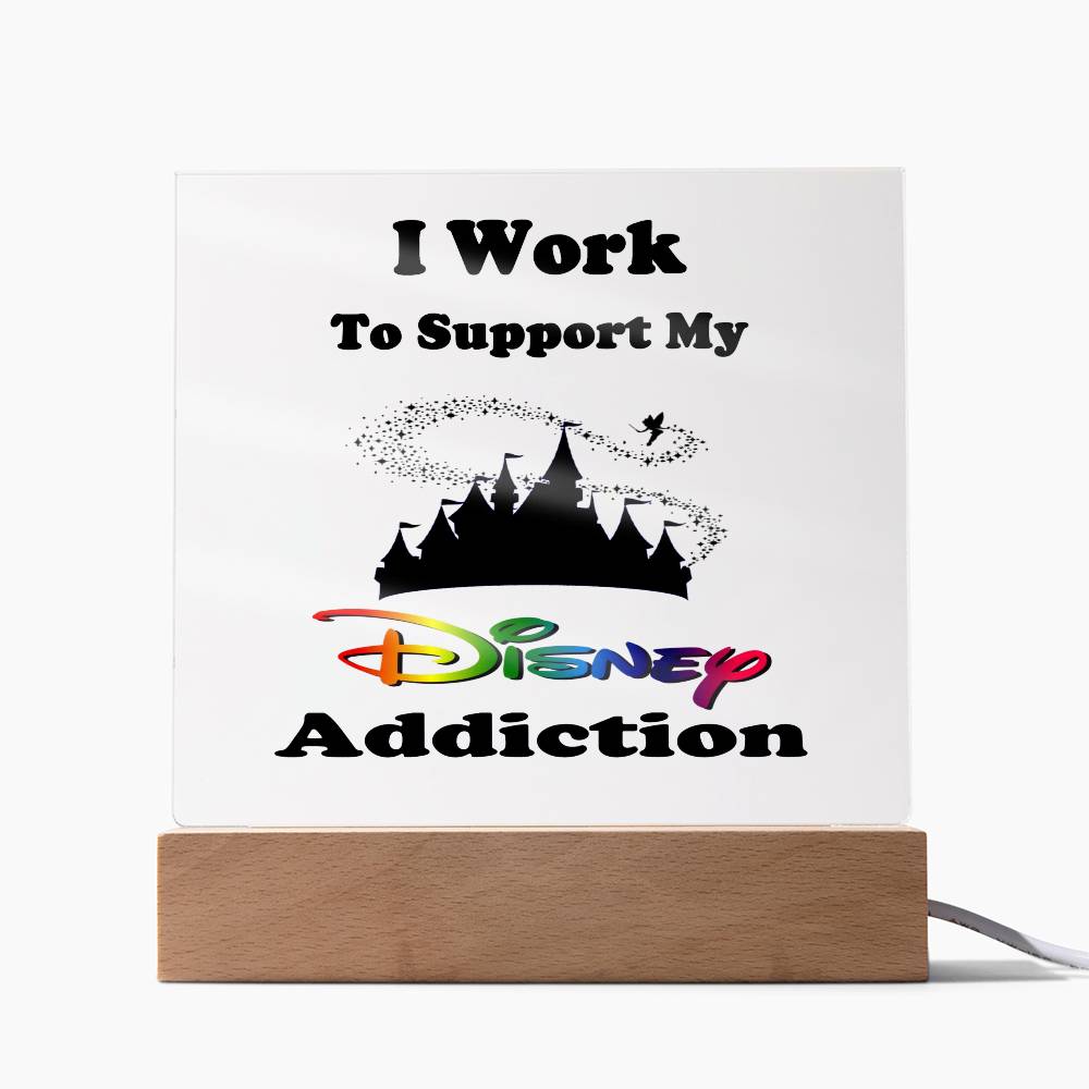 The Disney Obsessed plaque by ShineOn Fulfillment displays the phrase, "I Work To Support My Disney Addiction," on an acrylic surface with a wooden base. It includes a silhouette of the Magic Kingdom castle and rainbow-colored lettering for "Disney," making it an ideal piece for any Disney enthusiast.