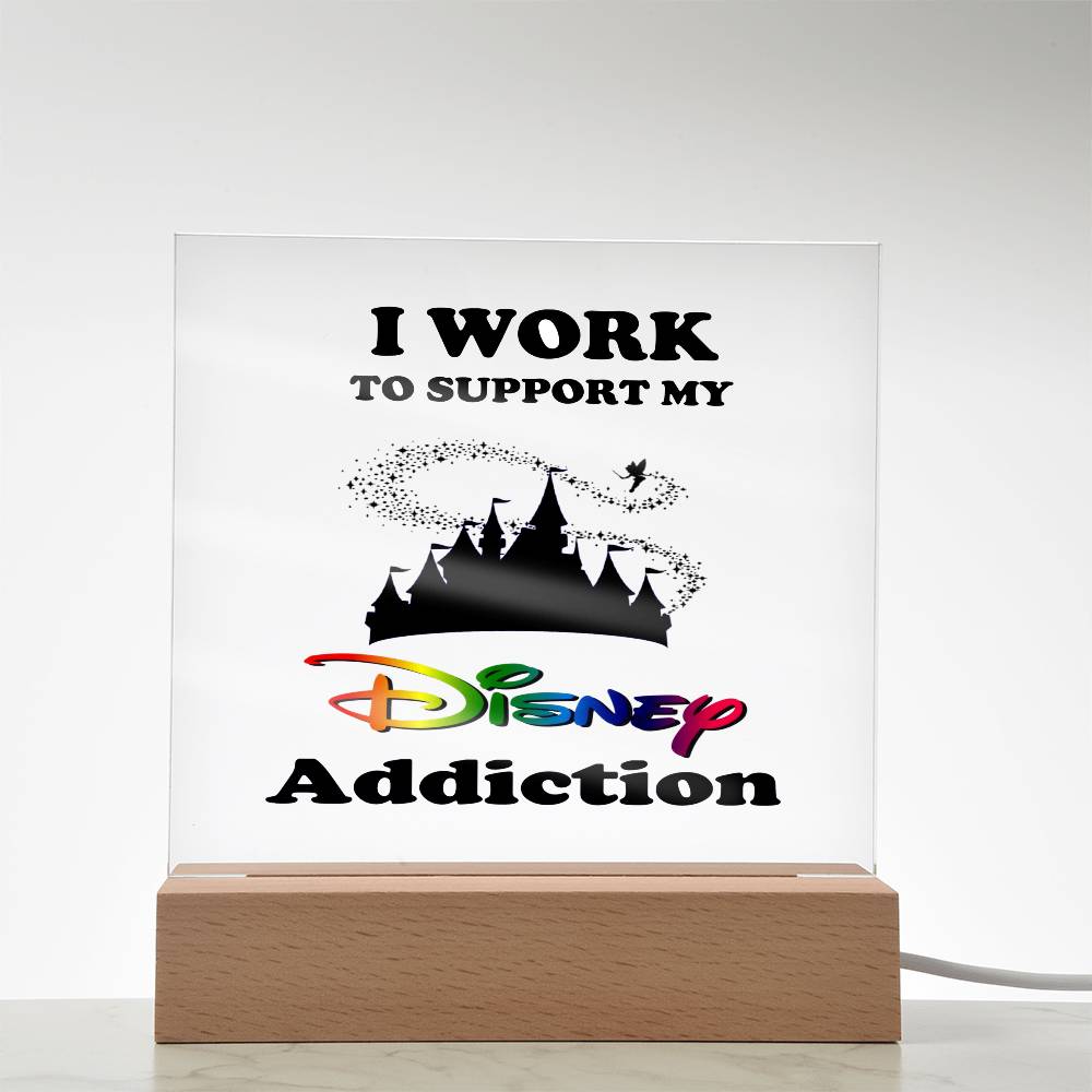 For the true Disney fan, the "Disney Obsessed: Where Magic Meets Everyday Life!" light box by ShineOn Fulfillment features a whimsical design with the text: "I work to support my Disney addiction." It showcases a silhouette of a castle adorned with pixie dust and a small flying figure. The enchanting acrylic plaque is complemented by its charming wooden base.