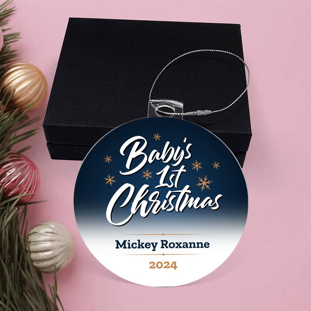 A personalized acrylic ornament titled "Twinkling Joy: Baby's First Magical Christmas" from ShineOn Fulfillment, featuring the engraving "Baby's 1st Christmas, Mickey Roxanne, 2024," sits on a pink surface next to a black box. Nearby are pine branches adorned with red, gold, and silver baubles. This special ornament makes for a unique keepsake.