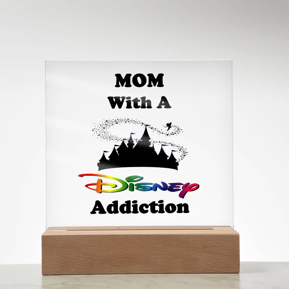 An acrylic plaque from ShineOn Fulfillment, titled "Disney-Obsessed Mom: Where Magic Meets Motherhood!", features bold text with the phrase "MOM With A Disney Addiction." The word "Disney" is styled in the iconic logo font. Atop, a silhouette of the Magic Kingdom castle is enhanced by Tinkerbell sprinkling pixie dust.