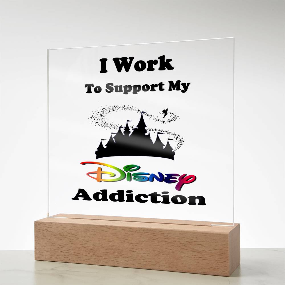 Introducing the "Disney Obsessed: Where Magic Meets Everyday Life!" by ShineOn Fulfillment – an acrylic plaque featuring the bold phrase "I Work to Support My Disney Addiction" alongside a silhouette of the Magic Kingdom castle and vibrant Disney logo elements. This exquisite piece is beautifully displayed on a wooden base against a simple backdrop.