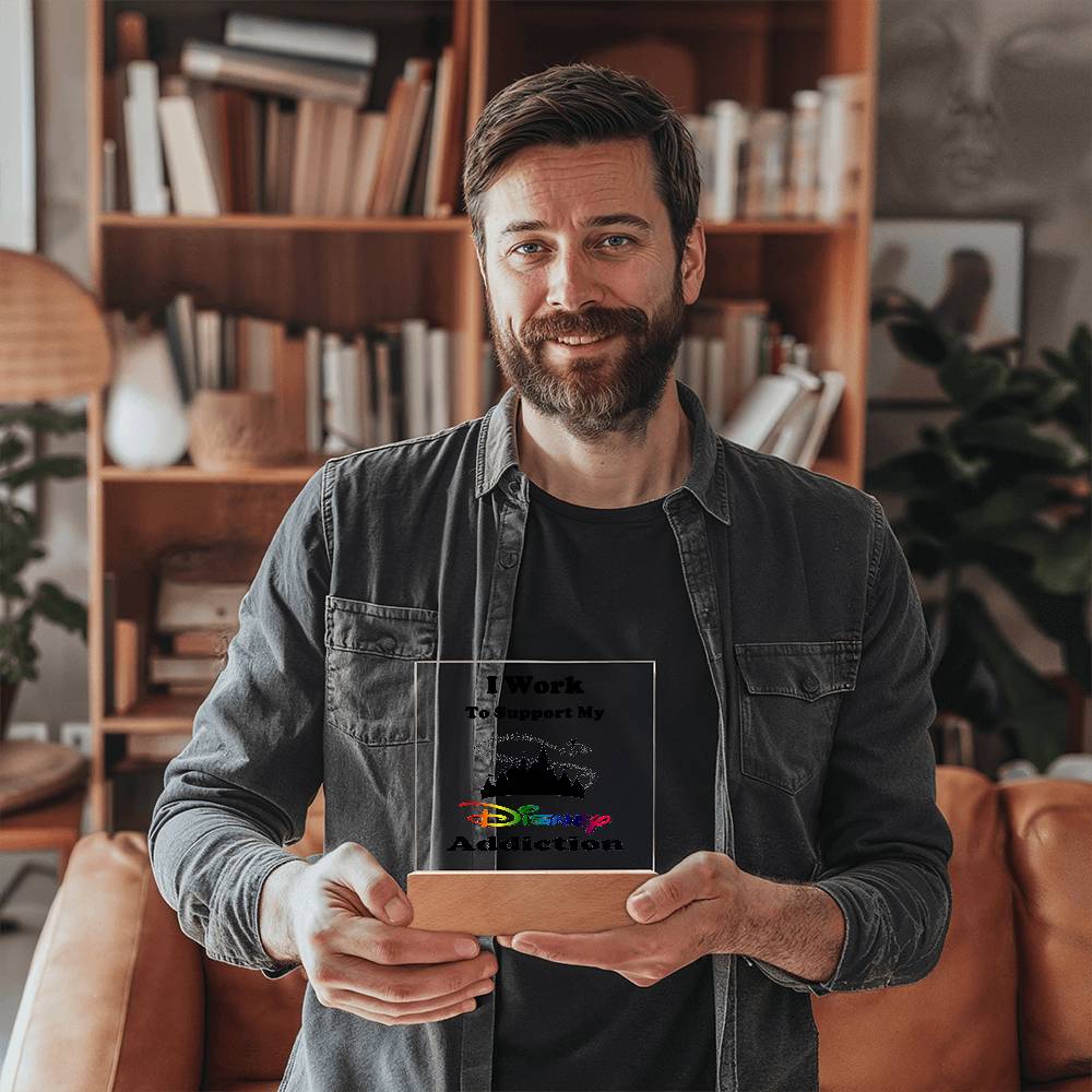 A man sporting a beard and a casual shirt is holding the Disney Obsessed: Where Magic Meets Everyday Life! plaque by ShineOn Fulfillment. He smiles in front of shelves filled with books and decor items in the background.