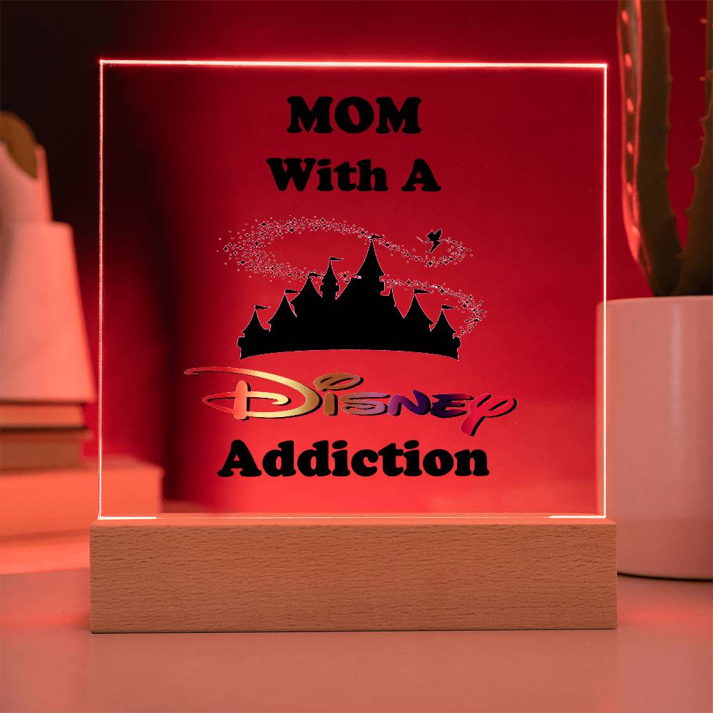 This glowing acrylic plaque from ShineOn Fulfillment, titled "Disney-Obsessed Mom: Where Magic Meets Motherhood!", makes a perfect gift for moms. It features the text "MOM With A Disney Addiction" in black with the iconic Disney castle silhouette and stylized font. The red background enhances its charm, accompanied by stacked books and a nearby cactus on its wooden base.