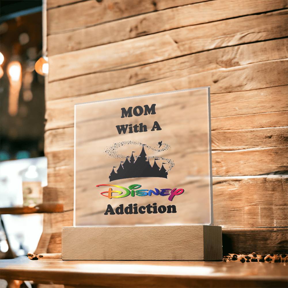 A captivating acrylic plaque from ShineOn Fulfillment, named "Disney-Obsessed Mom: Where Magic Meets Motherhood!", artistically showcases "MOM With A Disney Addiction" in lively text. Adorned with the iconic Disney castle silhouette, it sits enchantingly against a rustic wooden wall, capturing the whimsical spirit of Disney.